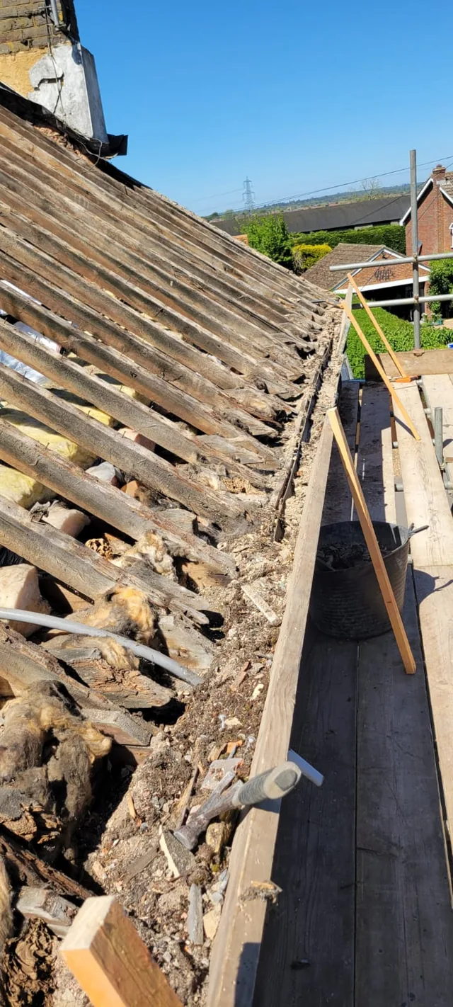 Deteriorated roof timbers and debris line the eaves above a scaffold walkway.