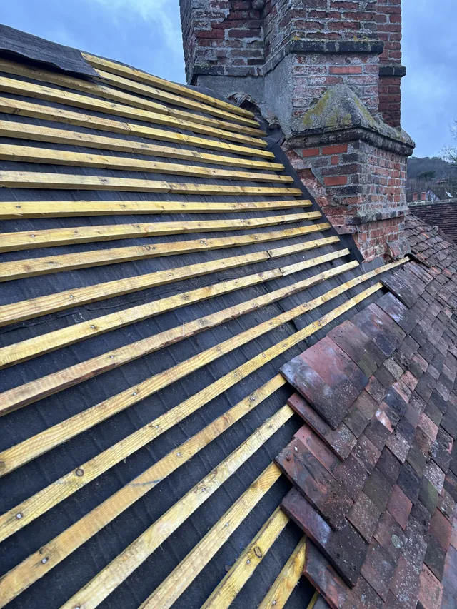 Yellow roof battens meet a stepped brick chimney beside partly laid reddish tiles.