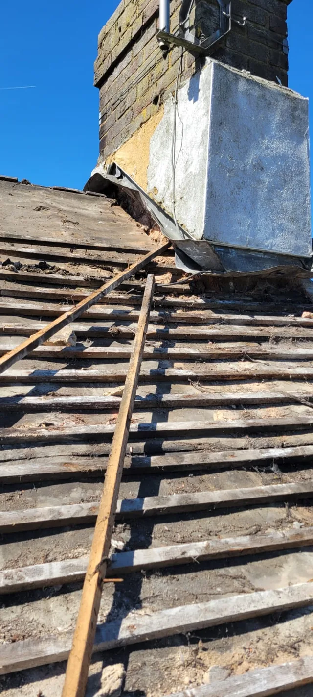 A rendered chimney base meets exposed old roof battens beside a wooden ladder.
