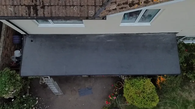 Overhead view of a dark flat extension roof beside cream walls and garden planting.