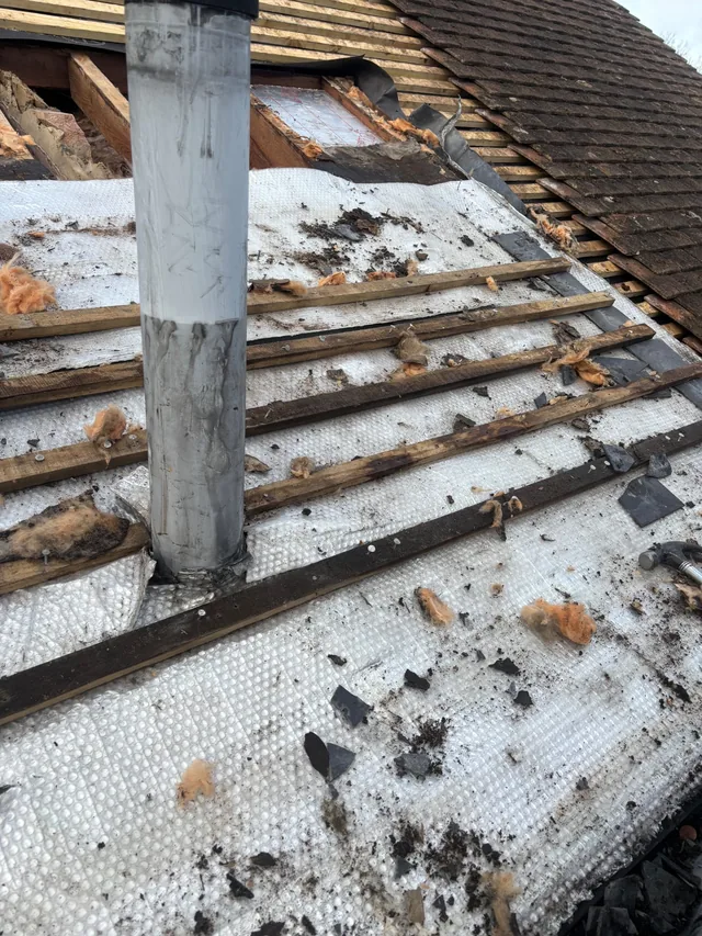 Tile fragments and old battens lie across white roof panels beside a scaffold pole.
