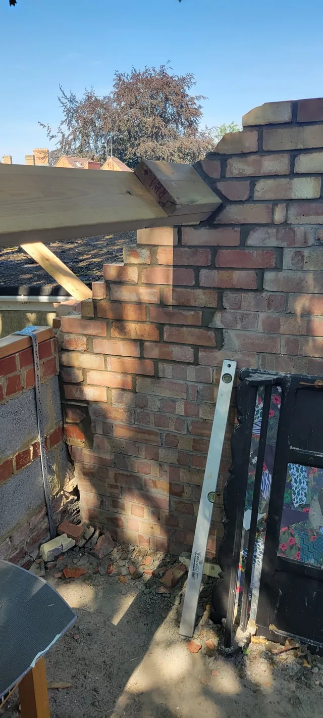 A timber purlin rests on new brickwork above stored doors and a spirit level.