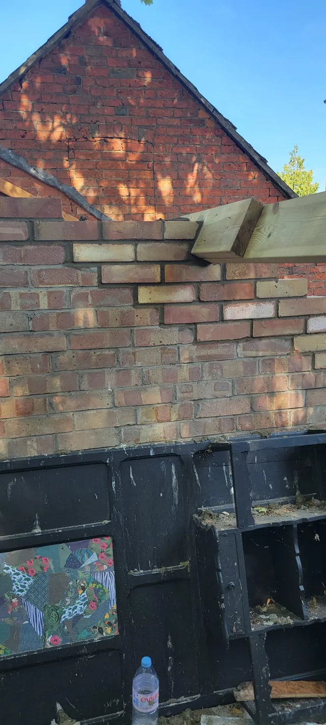 Fresh brick courses support a timber beam in front of a red brick gable.