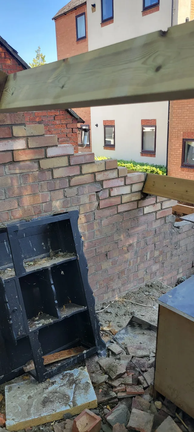 Large timber beams span an opening above partly rebuilt brickwork and stored doors.