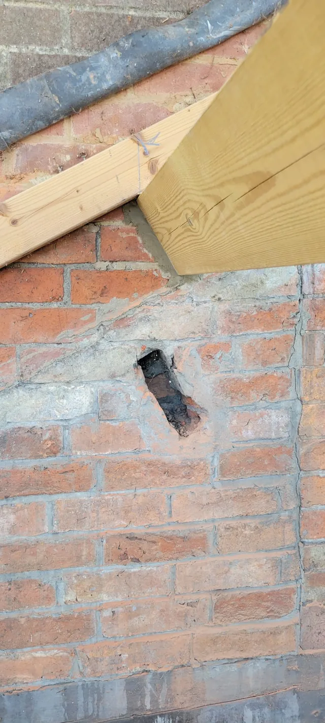 A new timber beam meets brickwork beneath flashing beside an old wall opening.