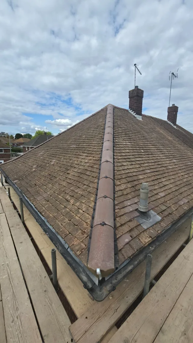 New brown hip caps divide cleaned roof slopes beside a flue and brick chimneys.