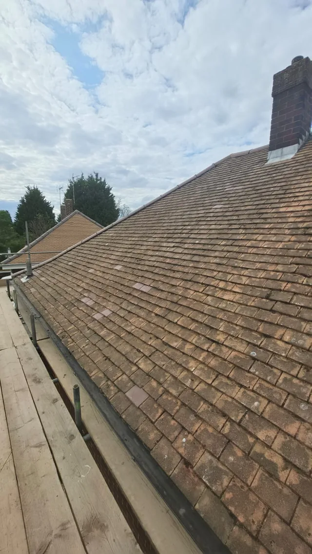 A broad brown tiled slope appears cleared of loose moss beside a scaffold walkway.