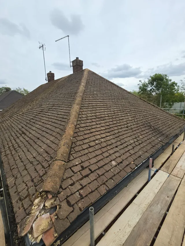 Weathered brown roof tiles meet a mossy hip above a gutter and scaffold boards.