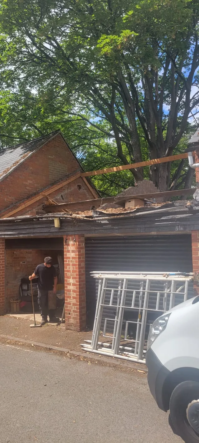 A roofer stands below an opened garage roof beside ladders and a parked van.