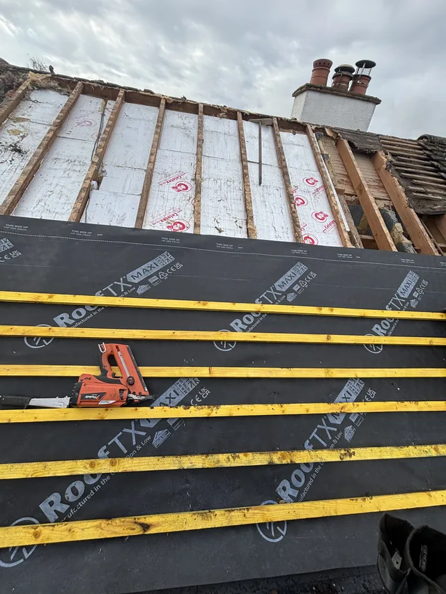 Yellow battens cross dark membrane below exposed white panels and a rendered chimney.