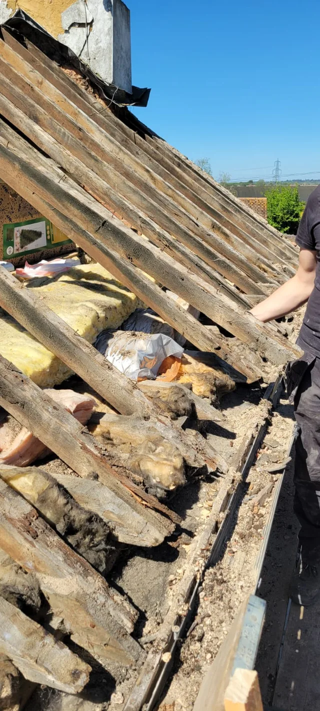 A roofer handles an old timber beside exposed roof framing and loose insulation.