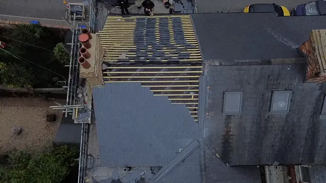 An overhead roof view shows partly laid grey slates alongside exposed yellow battens.