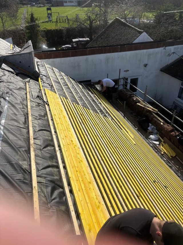 A steep roof is lined with yellow battens while roofers work beside scaffolding.