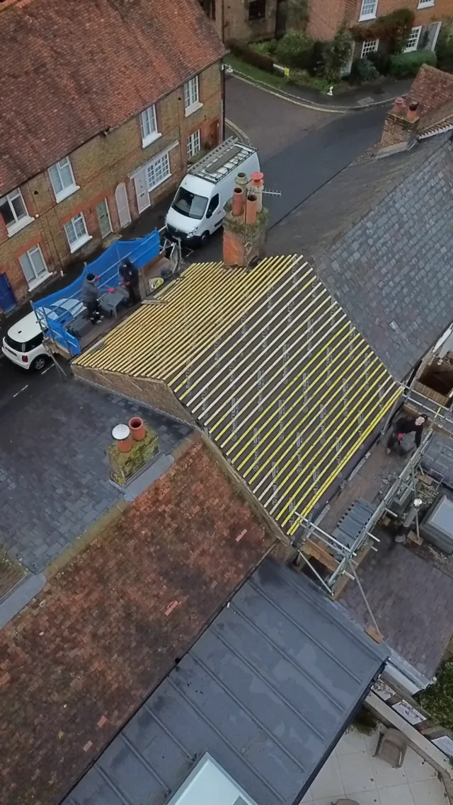Overhead view of yellow roof battens beside a chimney and parked vehicles below.