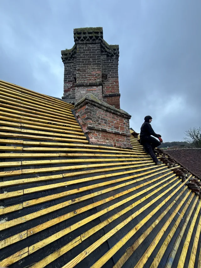 A roofer sits beside a brick chimney above newly fitted yellow roof battens.