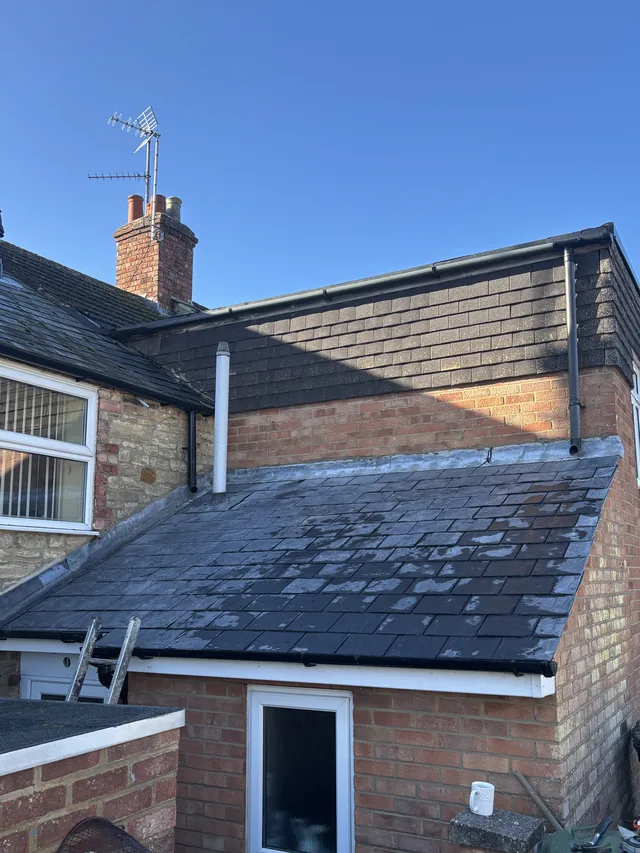 Dark slates cover a small extension beneath brickwork, wall tiles and white drainage pipes.