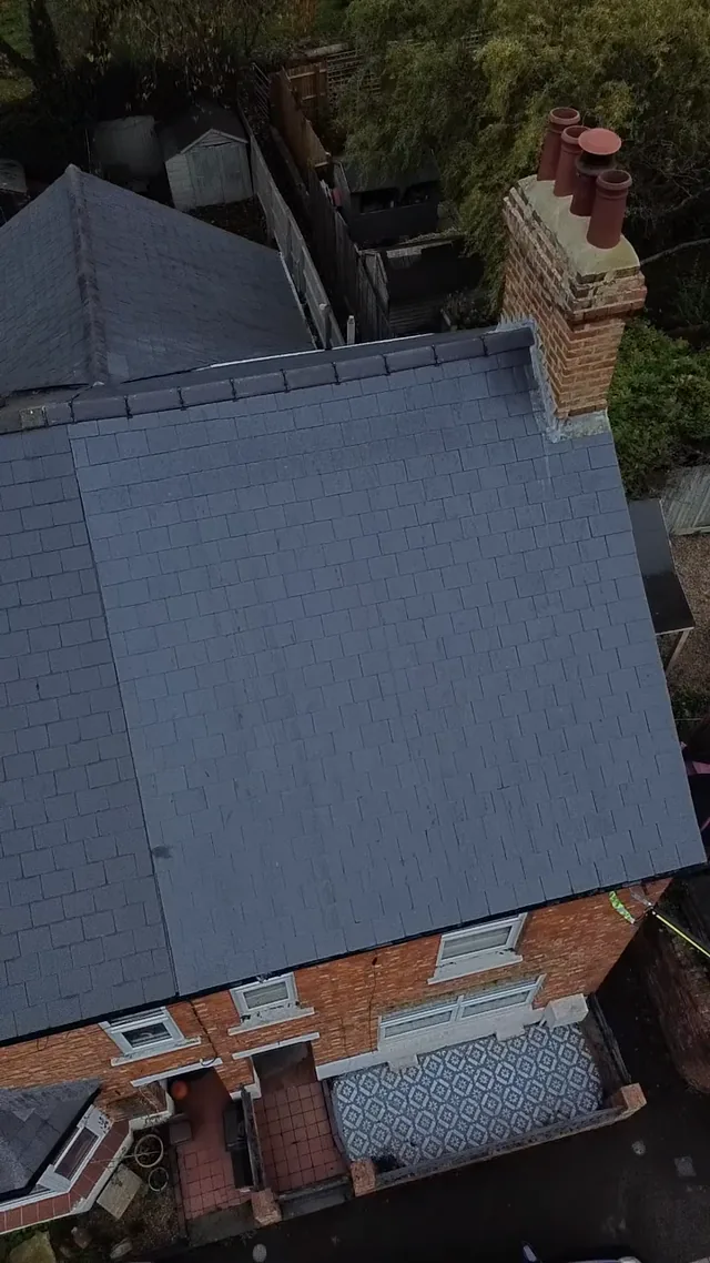 Grey roof slates meet a ridge and brick chimney above a patterned front path.