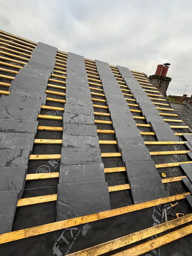 Three narrow runs of grey slates extend upwards across exposed yellow roof battens.