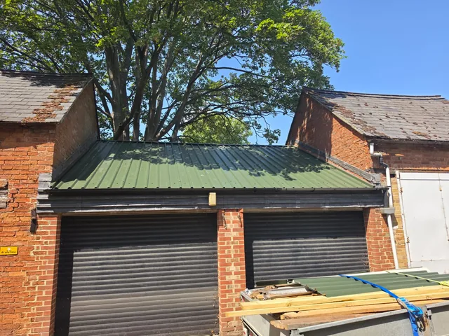 Green profiled sheets cover a double garage beneath trees, with spare materials stacked outside.