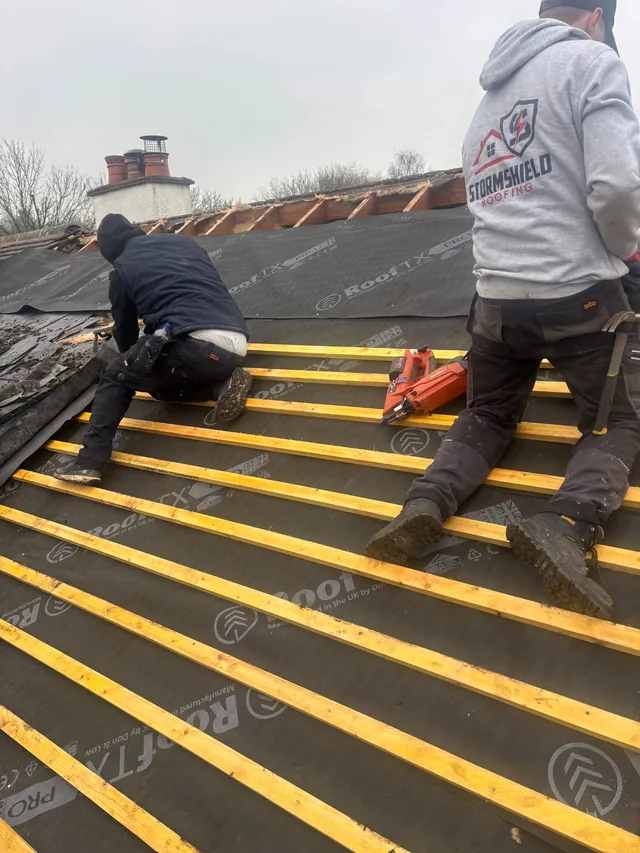 Two roofers work on yellow battens, one wearing a grey Stormshield hoodie.