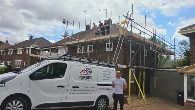 Four roofers pose beside a signwritten Stormshield van and on scaffolding around a house.