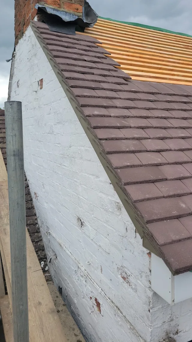 Brown tiles cover a cottage gable edge beside exposed battens and a brick chimney.