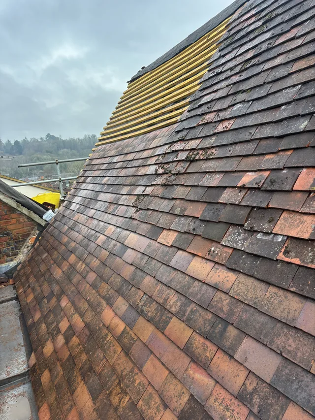 Reddish plain tiles cover most of a roof slope below exposed yellow battens.
