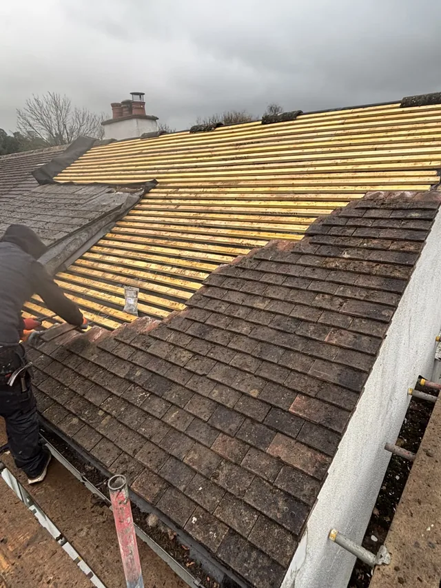 Old brown tiles form stepped edges beside new yellow battens and a roofer.